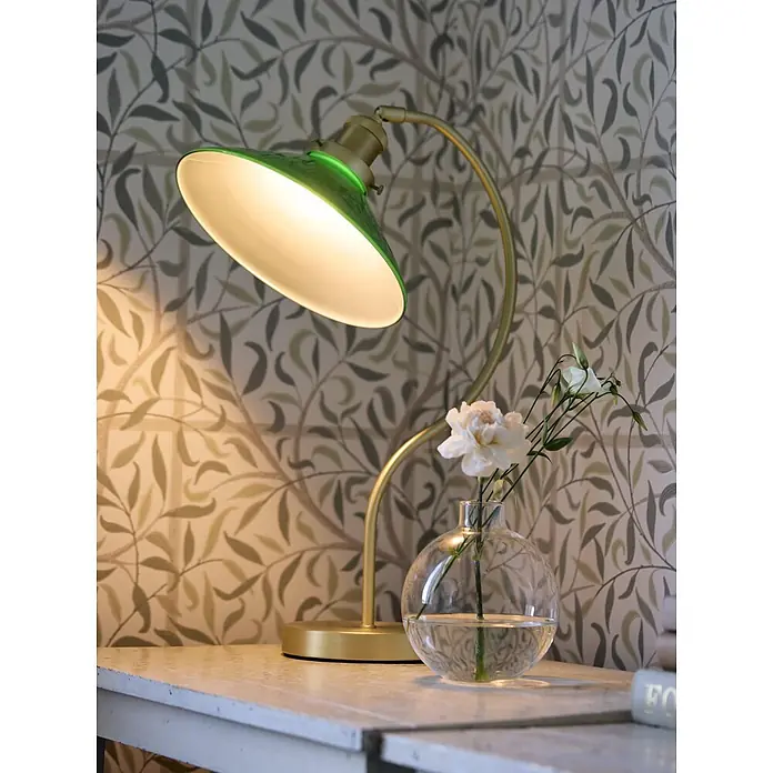 PR Home Tischleuchte Axel - 15 W, E27 - Goldene Schreibtischlampe mit grünem Schirm, wirft warmes Licht auf einen Tisch mit Blumen.