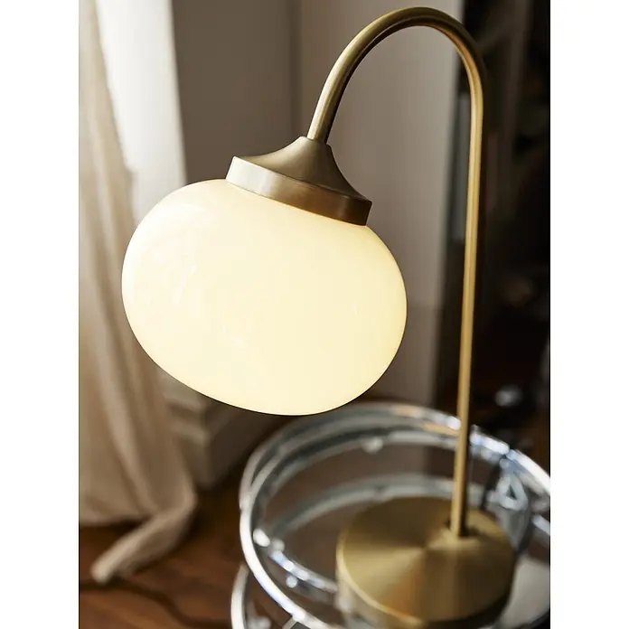 PR Home Tischleuchte Elsy - 240 W, E14 - Beleuchtete Messing-Tischlampe mit opalem Glasschirm, spendet warmes Licht auf einem Tisch.