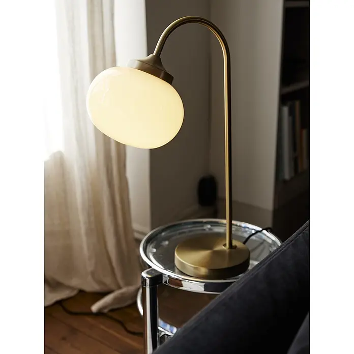 PR Home Tischleuchte Elsy - 240 W, E14 - Messing-Tischlampe mit Opalschirm, beleuchtet einen Wohnbereich neben einem Sofa.