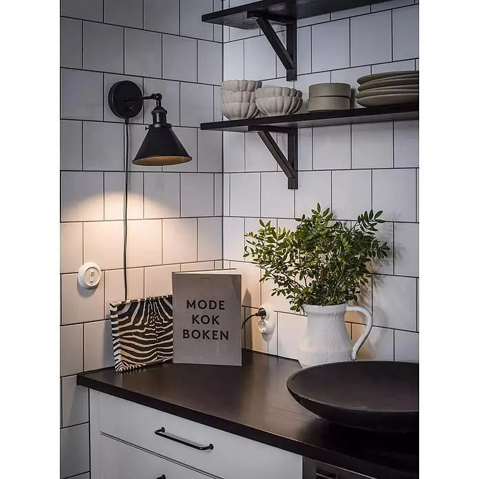 PR Home Wandleuchte Anton - 25 W, E27 - Schwarze Wandlampe mit konischem Schirm beleuchtet eine gestaltete Küchenecke.