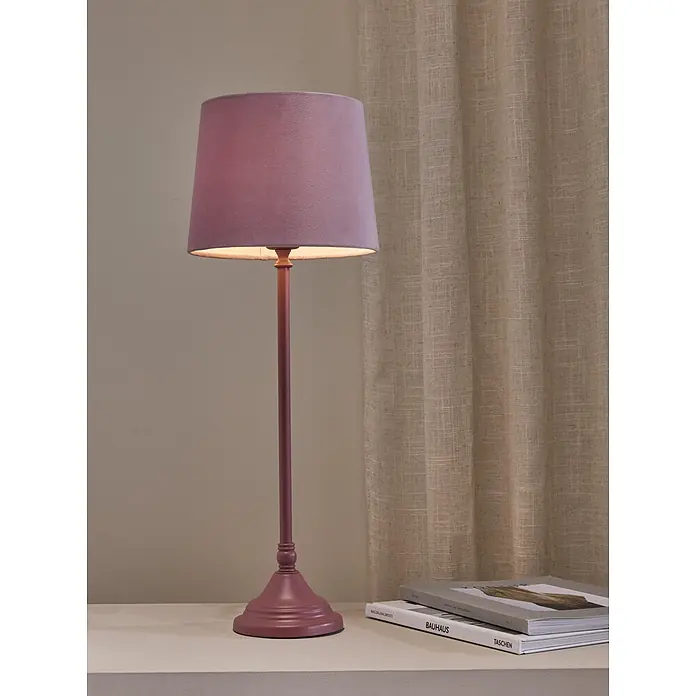 PR Home Tischleuchte Tove - 40 W, L x B x H: 20 x 20 x 57 cm, E27 - Lila Tischlampe mit Stoffschirm, beleuchtet Bücher auf einer weißen Oberfläche.