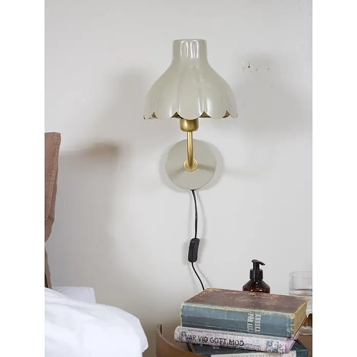 PR Home Wandleuchte Wells - 25 W, E27 - Helle graue Wandleuchte mit Muschelrand und Messingarm über einem Nachttisch als Leselampe.