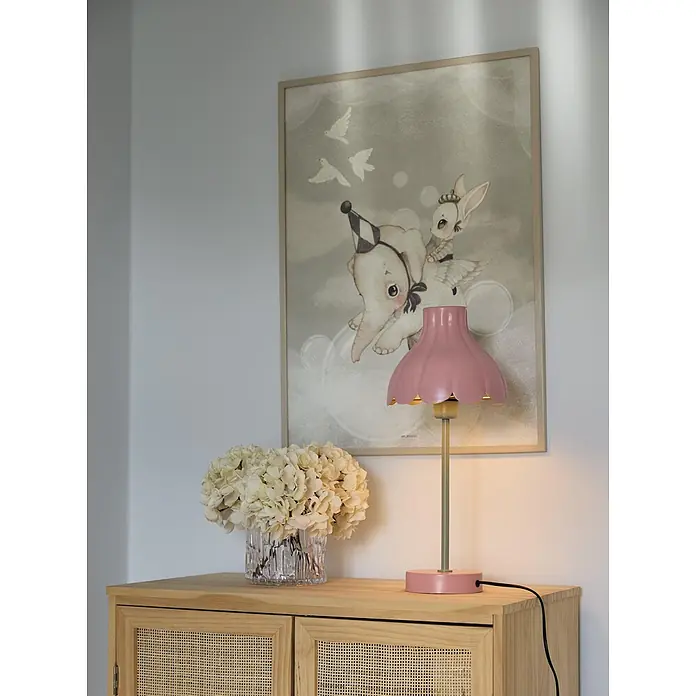 PR Home Tischleuchte Wera - 25 W, E27 - Rosa geriffelte Tischleuchte mit gedämpft goldenem Stiel und rosa Sockel, die ein Holzschränkchen beleuchtet.