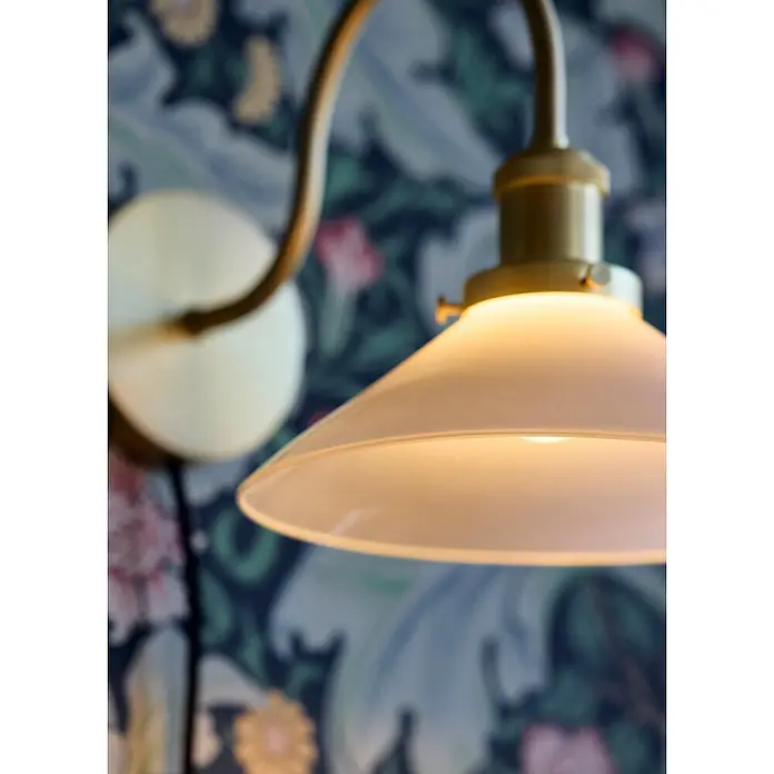PR Home Wandleuchte Axel - 15 W, E27 - Messing-Wandleuchte mit mattem Glasschirm, die warmes Licht abstrahlt, montiert an einer gemusterten Wand.