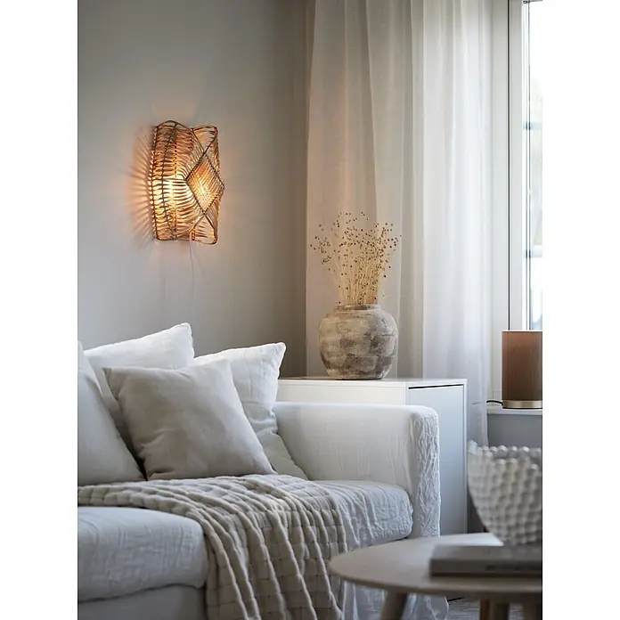 PR Home Wandleuchte Wandleuchte Zyla - 15 W, E14 - Geflochtene Rattan-Wandleuchte mit warmem Licht, an einer hellen Wand über einem Sofa in einem gemütlichen Wohnzimmer montiert.
