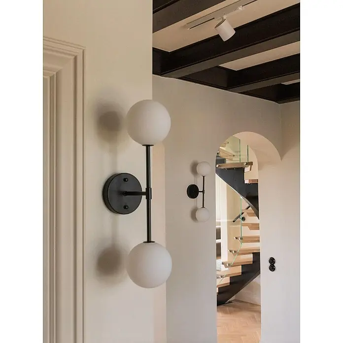 PR Home Wandleuchte Wandleuchte Sigma D - 25 W, G9 - Zwei moderne Wandleuchten mit schwarzen Rahmen und kugelförmigen weißen Glasdiffusoren, in einem Flur mit Treppe installiert.