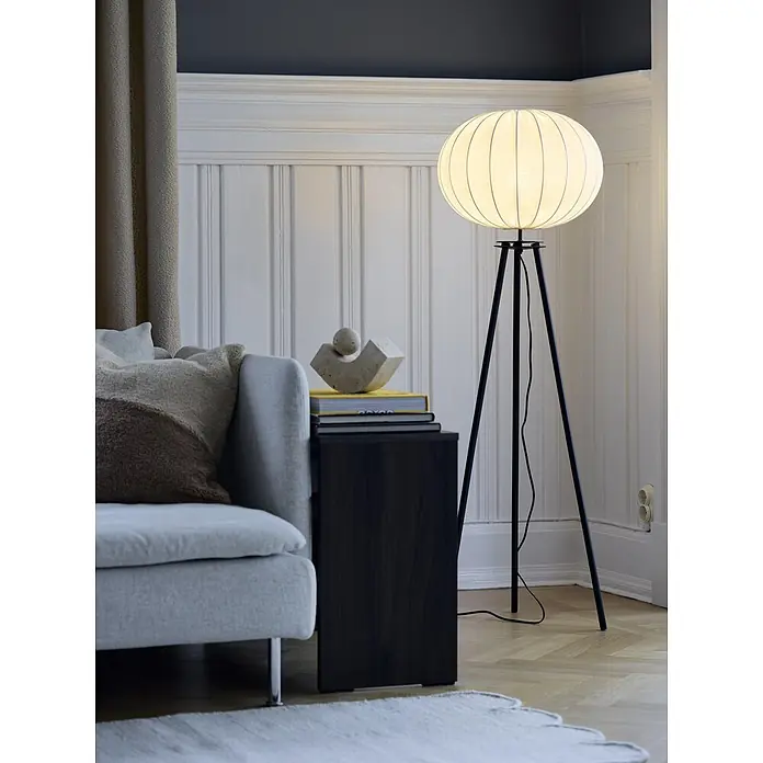 PR Home Stehleuchte schwarz - 40 W, E27 - Eine moderne Stehlampe mit rundem, hellem Stoffschirm und schwarzem Dreibeingestell steht im Wohnzimmer neben einem Sofa.