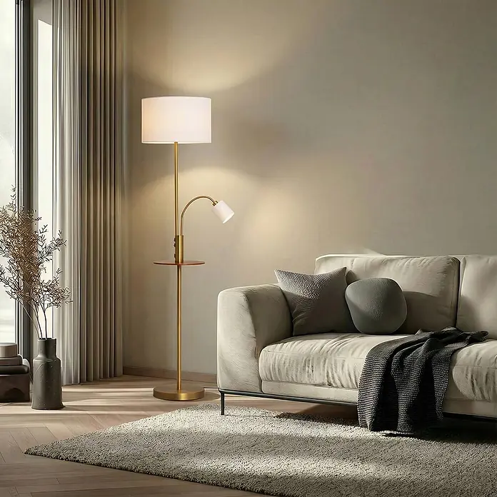 Lindby Stehleuchte Aovan - Höhe: 170 cm, bronze / altmessing, creme / amber, E27 - Goldene Stehlampe mit weißem Hauptschirm, verstellbarer Leselampe und integriertem Beistelltisch neben einem hellen Sofa.