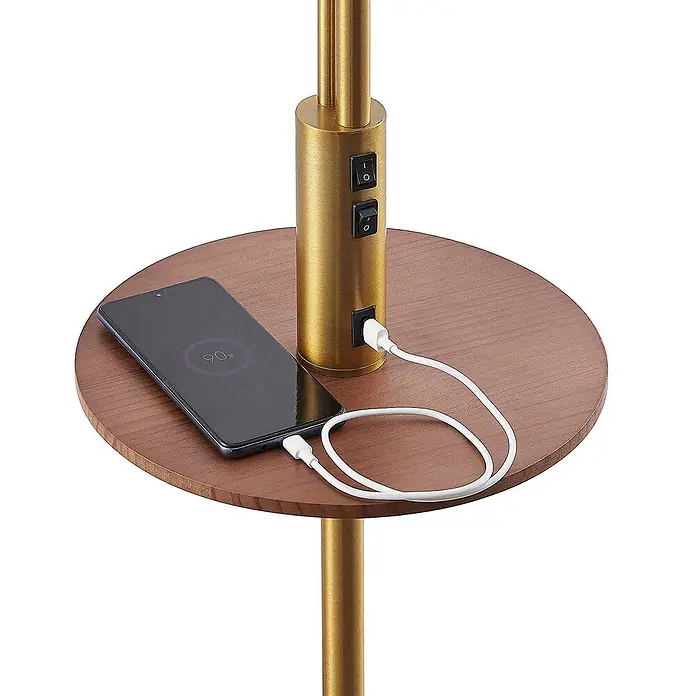Lindby Stehleuchte Aovan - Höhe: 170 cm, bronze / altmessing, creme / amber, E27 - Goldene Stehlampe mit brauner Holzablage, USB-Anschluss und Schaltern. Ein Smartphone lädt auf der Ablage.
