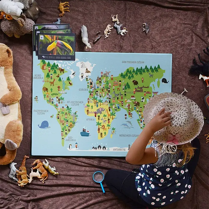 LanaKK Leinwandbild - Weltkarte, B x H: 100 x 70 cm - Kind interagiert mit einer farbenfrohen, illustrierten Weltkarte für Kinder, die Kontinente, Tiere und deutsche Beschriftungen zeigt.