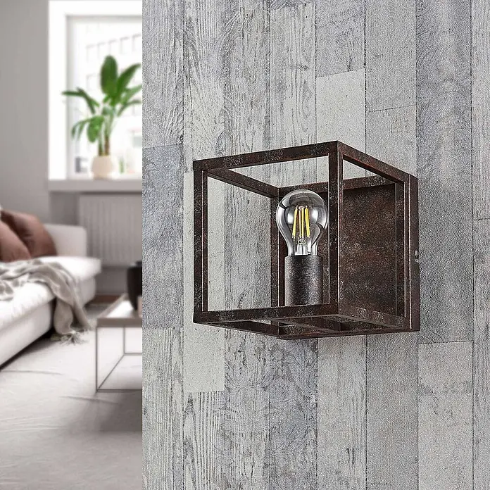 Lindby Wandleuchte Emin - braun / rost, braun / rost, E27 - Rostbraune Metall-Wandleuchte in Würfelform mit sichtbarer Edison-Glühbirne, an einer strukturierten Wand im Wohnzimmer montiert.