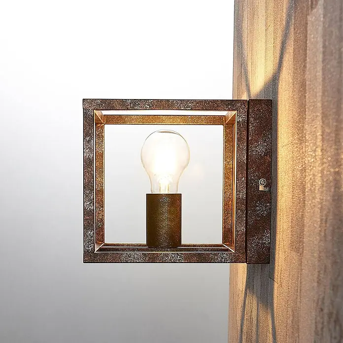 Lindby Wandleuchte Emin - braun / rost, braun / rost, E27 - Quadratische Wandlampe mit Altkupfer-Finish und sichtbarer Glühbirne, an einer strukturierten Wand.