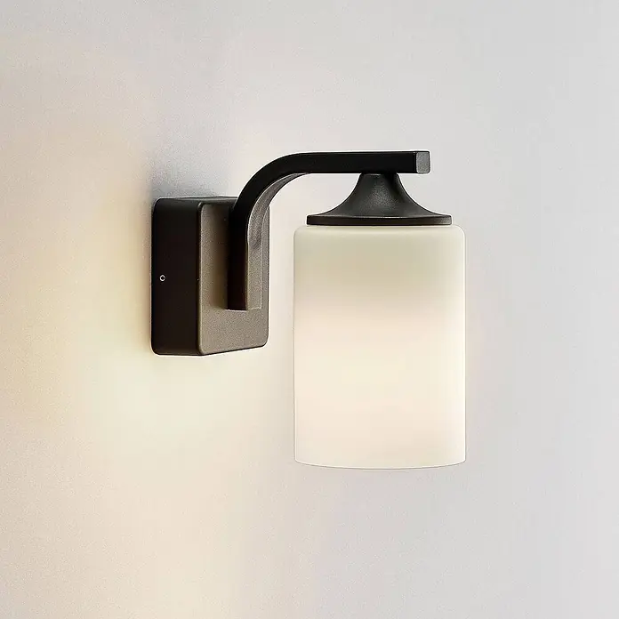 Lindby Außenwandleuchte Yannis - 21 x 11,8 x 21,2 cm, alu / grau / zink, creme / amber, IP43 - Mattschwarze Wandleuchte mit gebogenem Arm und mattweißem zylindrischen Glasschirm, strahlt warmes Licht aus.