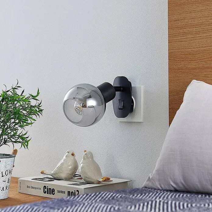 Lindby Wandleuchte Lioma - L x B x H: 18,5 x 9 x 14,5 cm, schwarz, schwarz, E14 - Schwarze Stecklampe mit rauchfarbenem, kugelförmigem Glasschirm und integriertem Schalter, als Nachttischleuchte verwendet.
