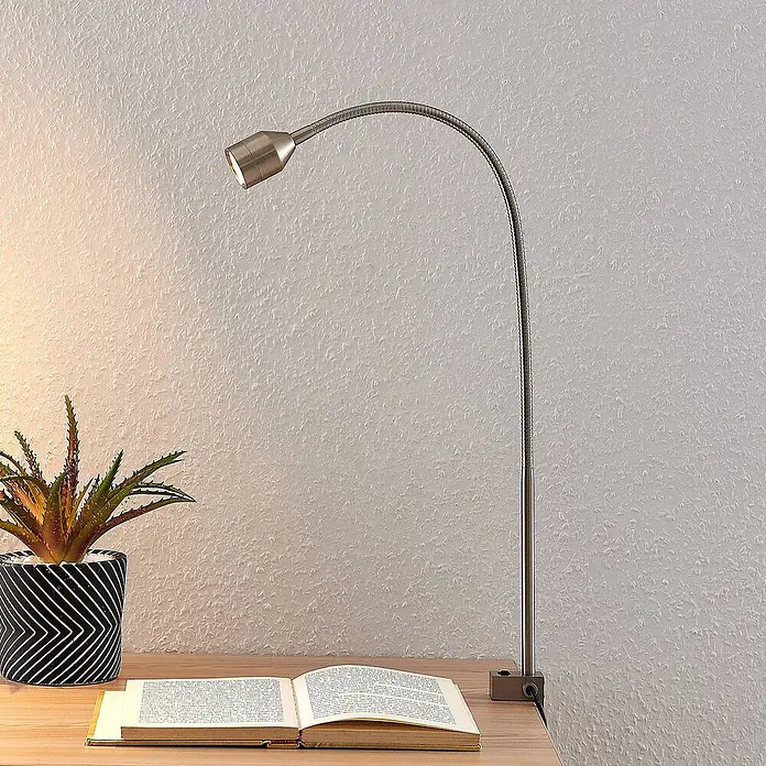 Lindby Klemmleuchte Hanilo - L x B x H: 37 x 4 x 80 cm, Farbe Gehäuse: alu / grau / zink - Gebürstete Metall-Klemmleuchte mit Schwanenhals und LED-Licht, beleuchtet ein offenes Buch auf Holzschreibtisch neben Pflanze.