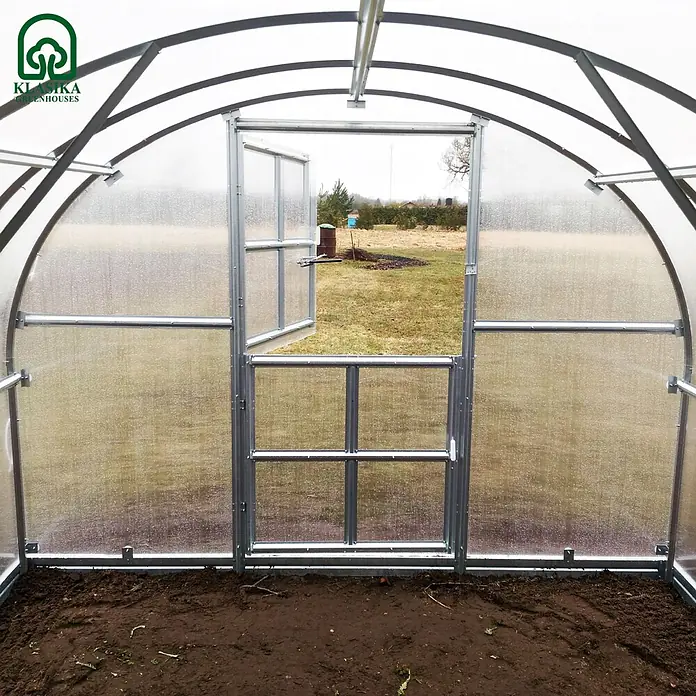Klasika Greenhouses Gewächshaus Arch Klasika - Außenmaß inkl. Dachüberstand (B x T): 300 x 400 cm, Material Seitenwand: Kunststoff, 4 mm, Silbergrau - Innenansicht eines Bogengewächshauses mit silbernem Metallrahmen, transparenten Platten und Erde. Tür zum Garten offen.