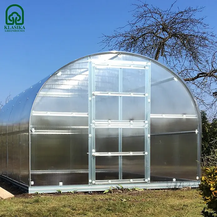 Klasika Greenhouses Gewächshaus Arch Klasika - Außenmaß inkl. Dachüberstand (B x T): 300 x 400 cm, Material Seitenwand: Kunststoff, 4 mm, Silbergrau - Ein gewölbtes Polycarbonat-Gewächshaus mit silbernem Metallrahmen, im Freien auf grünem Gras unter blauem Himmel installiert.