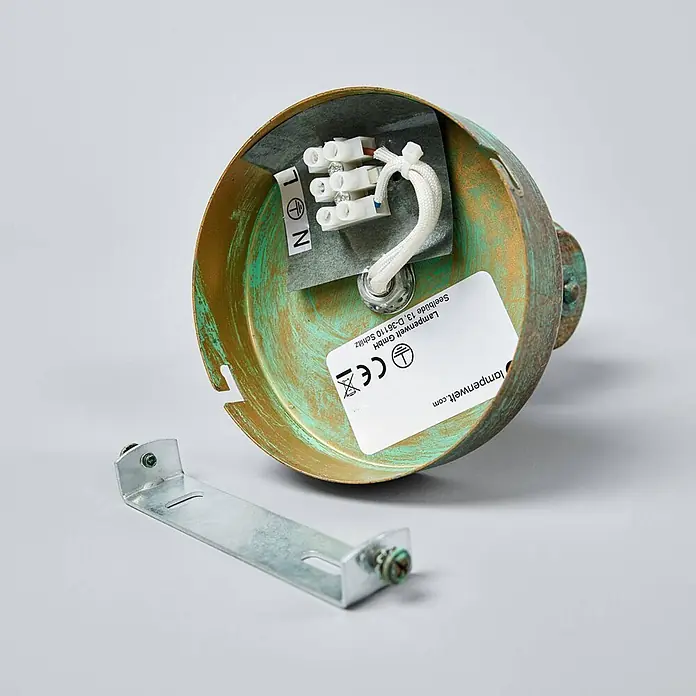 Lindby Wandleuchte Giorgi - bronze / altmessing, E14 - Innenseite einer verwitterten Bronze-Deckenrosette mit elektrischen Anschlüssen und Klemmenblock, neben einer Metallhalterung.
