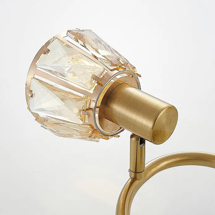Lindby Deckenleuchte Kosta - messing / gold, E14 - Gebürsteter goldener Scheinwerfer mit facettiertem Bernstein-Kristallschirm, montiert auf einem goldenen gebogenen Arm.