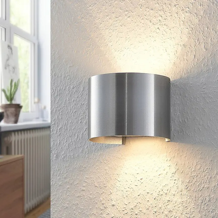 Arcchio Wandleuchte Zuzana - alu / grau / zink, G9 - Gebürstete Aluminium-Wandleuchte an einer strukturierten Wand, die warmes Licht nach oben und unten wirft.