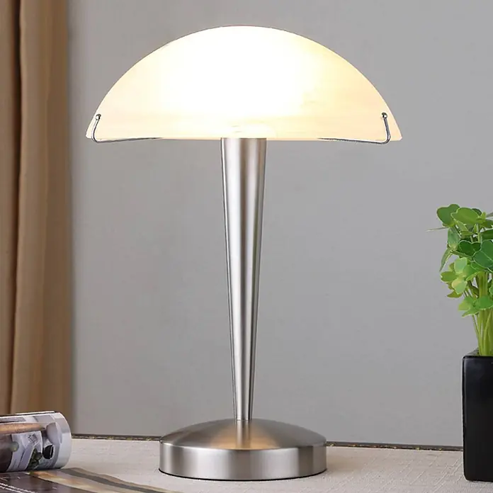 Lindby Tischleuchte Viola - L x B x H: 26 x 26 x 36 cm, alu / grau / zink, weiß / opal, E14 - Beleuchtete Tischleuchte mit gebürstetem Metallsockel und gewölbtem Milchglasschirm, auf einem Tisch platziert.