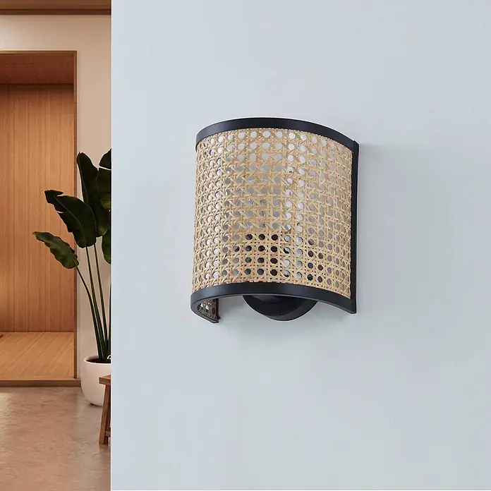 Lindby Wandleuchte Yaelle - Holz hell, E27 - Schwarze Wandleuchte aus natürlichem Rattan-Geflecht, die eine moderne Einrichtung beleuchtet.