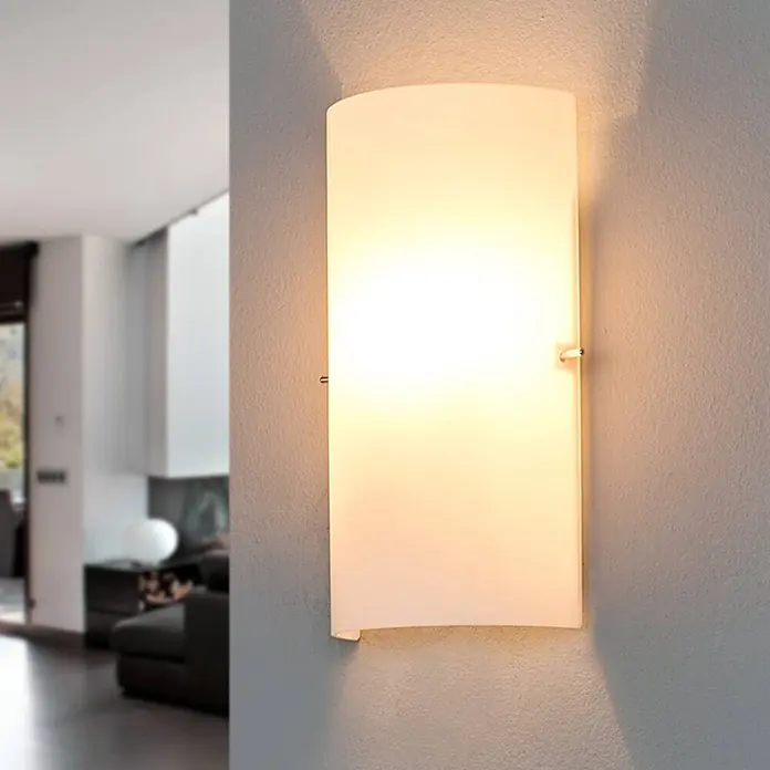 Lucande Wandleuchte Sidra - weiß / opal, E14 - Eine moderne, rechteckige, mattweiße Wandleuchte, die warmes Licht in einem Wohnzimmer ausstrahlt.
