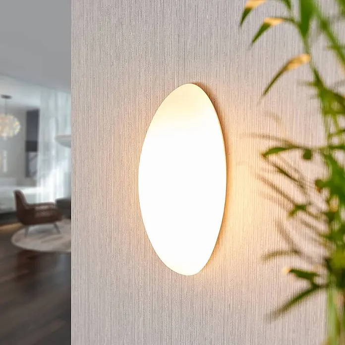 Lucande Wandleuchte Jemima - L x B x H: 8 x 12 x 24 cm, weiß / opal, E14 - Ovale Wandleuchte beleuchtet eine strukturierte Wand in einem modernen Wohnraum.