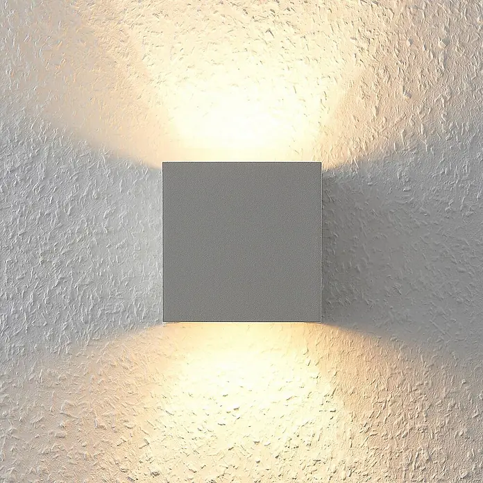 Arcchio Wandleuchte Zuzana - weiß / opal, G9 - Quadratische graue Wandleuchte beleuchtet eine strukturierte Wand mit warmen Auf- und Abwärtsstrahlen.