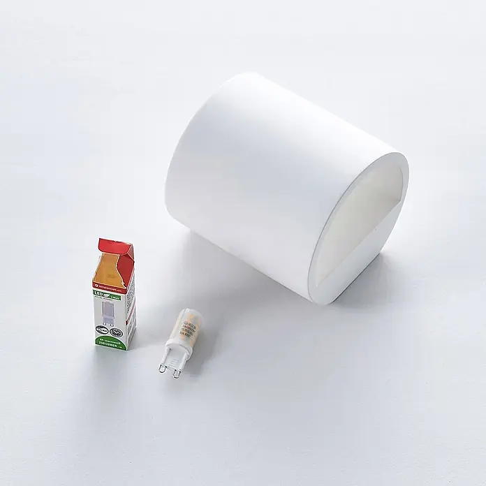 Lindby Wandleuchte Krista - L x B x H: 10 x 10,5 x 10 cm, weiß / opal, G9 - Weiße zylindrische Wandleuchte mit eckigem Ausschnitt, daneben eine kleine LED G9 Birne und ihre Verpackung.