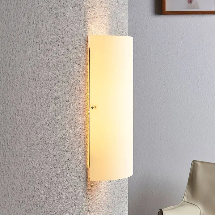Lindby Wandleuchte Tuli - L x B x H: 7,4 x 15 x 28 cm, weiß / opal, E14 - Mattweiße Glaswandleuchte, die warmes gelbes Licht spendet, an einer strukturierten Wand montiert.