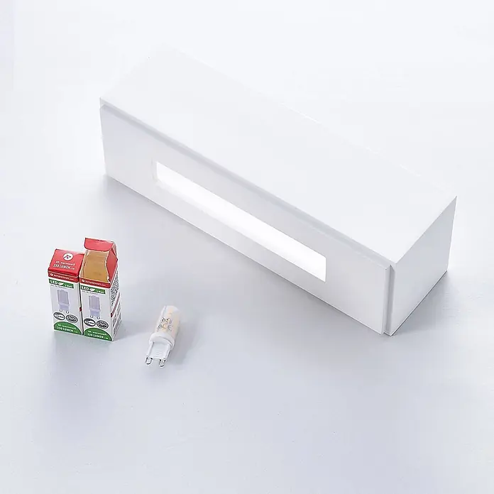 Lindby Wandleuchte Benno - L x B x H: 9 x 29 x 9 cm, weiß / opal, G9 - Weiße rechteckige LED-Wandleuchte mit beleuchtetem Schlitz, daneben eine G9-LED-Birne und deren Verpackung.