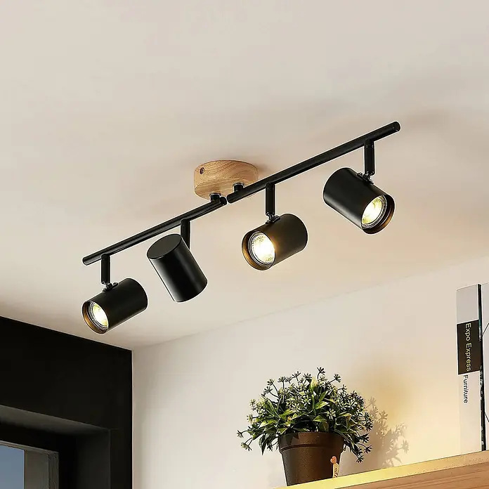 Lindby Deckenleuchte Xiomara - schwarz, GU10 - Eine schwarze Deckenstrahlleiste mit vier verstellbaren zylindrischen Lichtern und einer Naturholz-Montageplatte an einer weißen Decke.