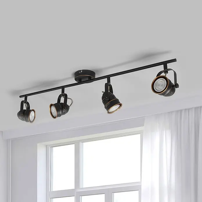 Lindby Deckenleuchte Leonor - schwarz, schwarz, GU10 - Schwarze Schienenleuchte mit 4 Strahlern und Bronzeakzenten, an der Decke über einem Fenster montiert.