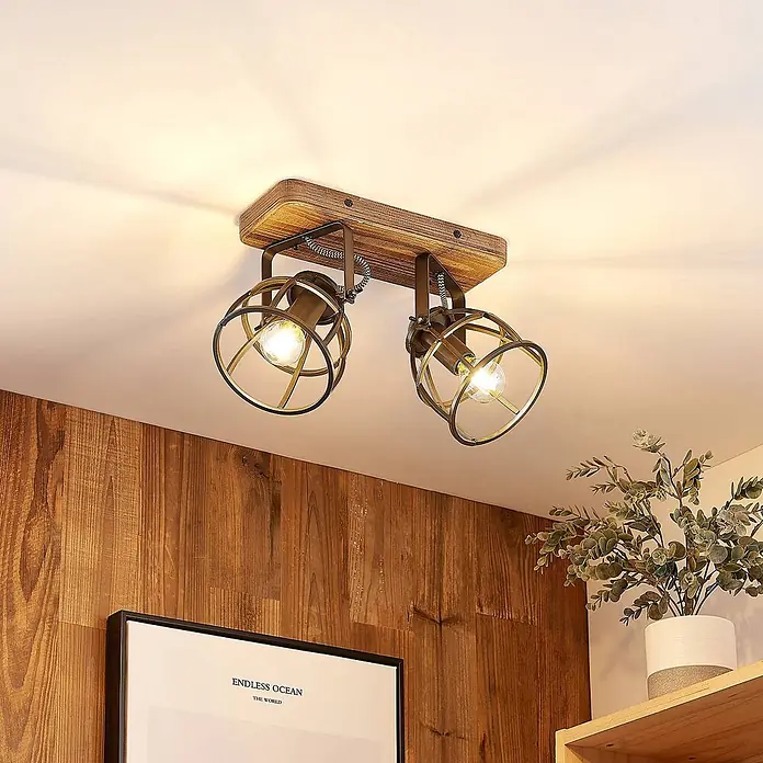 Lindby Deckenleuchte Rutger - Holz dunkel, schwarz, E14 - Deckenleuchte mit zwei Spots, rustikalem Holzsockel und antik-messingfarbenen Metallkäfigschirmen, an der Decke montiert.