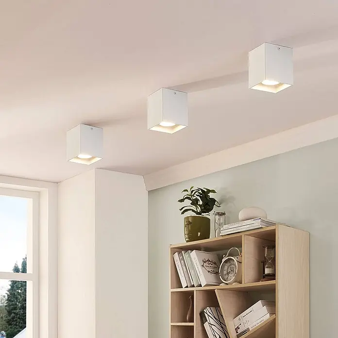 Arcchio Deckenleuchte Carson - weiß / opal, weiß / opal, GU10 - Drei weiße, würfelförmige Deckenleuchten erhellen ein modernes Zimmer mit Regal und hellgrünen Wänden.