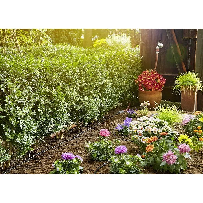 Gardena Micro-Drip Bewässerungs-Set Pflanzreihen Start-Set - Passend für: Pflanzreihen bis 15 m, Anwendungsbereich: Außen - Das Bild zeigt ein Bewässerungssystem in einem blühenden Garten mit Blumen und Pflanzen. Das System sorgt für eine effiziente Bewässerung.