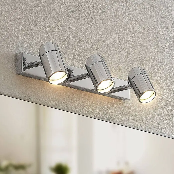 Lindby Deckenstrahler Remilan - chrom / silber, chrom / silber, GU10 - Verchromte dreiflammige Spiegelleuchte, montiert über einem Spiegel an einer strukturierten Wand.