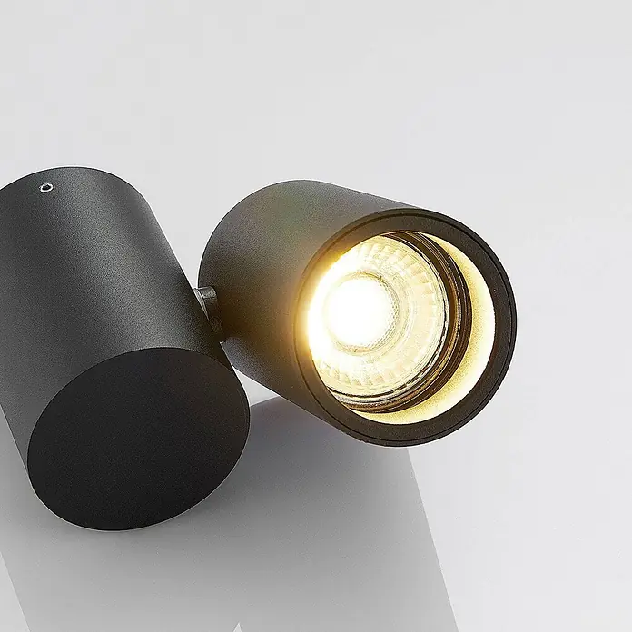 Arcchio Deckenstrahler Gesina - schwarz, schwarz, GU10 - Ein mattschwarzer, zylindrischer Doppel-LED-Strahler aus Metall, ein Kopf strahlt warmes Licht aus.