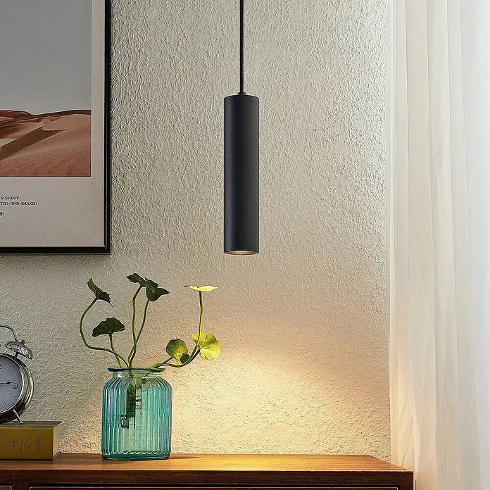 Prios Pendelleuchte Neliyah - L x B x H: 5,6 x 5,6 x 25 cm, schwarz, sandSchwarz, GU10 - Matte schwarze zylindrische Pendelleuchte, die warmes Licht auf eine Holzoberfläche wirft.