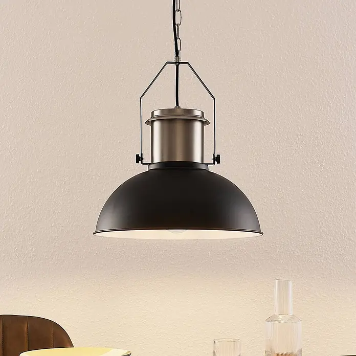 Lindby Pendelleuchte Freitjof - schwarz, Schwarz matt, nickel matt, E27 - Schwarze Industrie-Pendelleuchte mit gebürsteten Metalldetails über einem Tisch hängend.