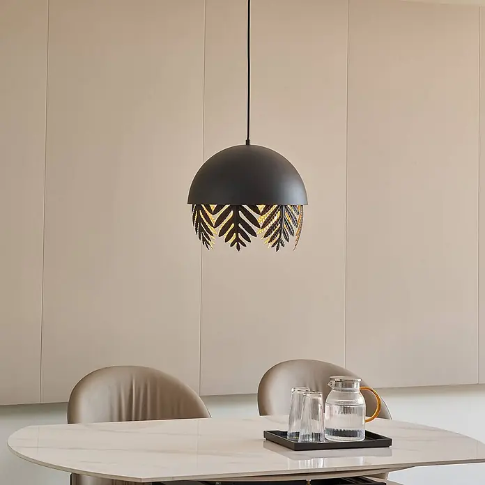 Lucande Pendelleuchte Aparas - schwarz, Schwarz, gold, E27 - Schwarze Metall-Hängeleuchte mit filigranem Blattausschnitt-Design, beleuchtet über einem modernen Esstisch hängend.