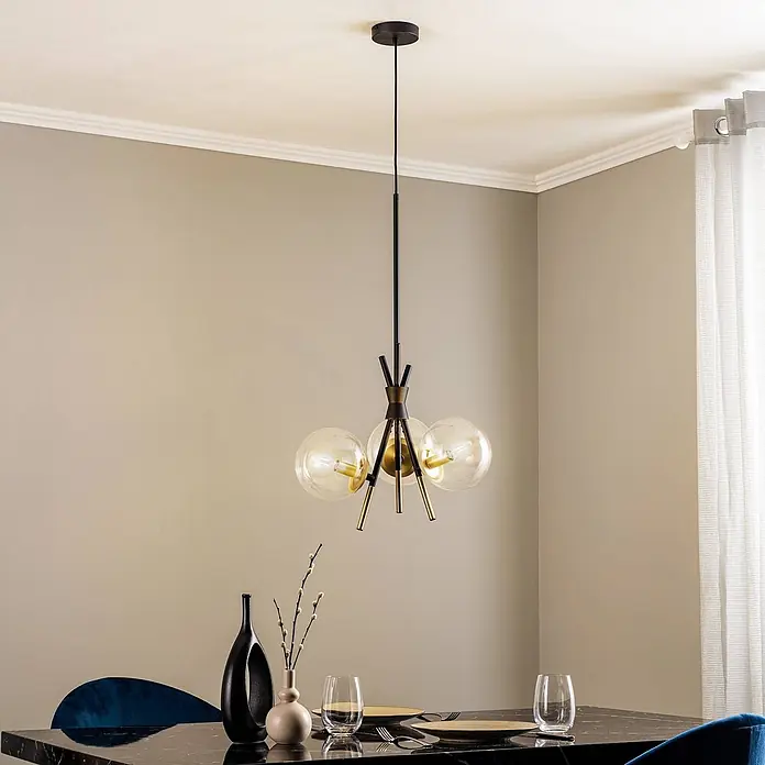Lucande Pendelleuchte Sotiana - klar, Schwarz, messing, E14 - Schwarz-goldener Kronleuchter mit drei klaren Glaskugeln, über einem Esstisch in einem modernen Raum hängend.