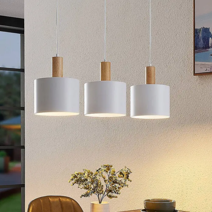 Lindby Pendelleuchte Kadir - L x B x H: 73 x 20 x 15 cm, weiß, holz, E27 - Drei Pendelleuchten mit zylindrischen weißen Schirmen und hellen Holzapplikationen über einem Esstisch.