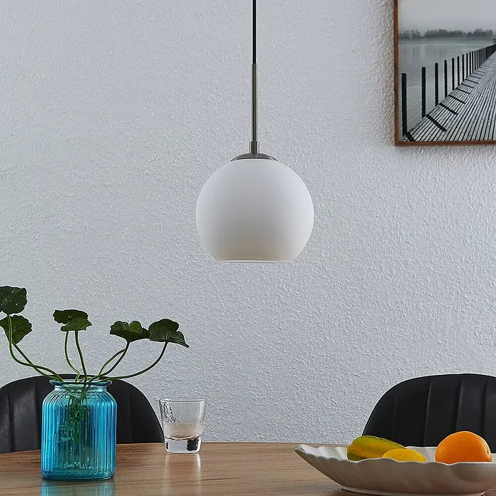 Lindby Pendelleuchte Jurian - L x B x H: 20 x 20 x 17,5 cm, weiß / opal, nickel, opal matt, E27 - Weiße kugelförmige Pendelleuchte hängt über einem Esstisch aus Holz.