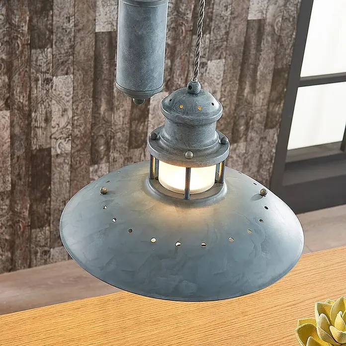 Lindby Pendelleuchte Louisanne - L x B x H: 35 x 35 x 25,7 cm, alu / grau / zink, grau-Grün, klar, E27 - Industrielle Hängelampe aus grauem Metall mit Schirm und Laternen-Detail, beleuchtet über einem Holztisch.