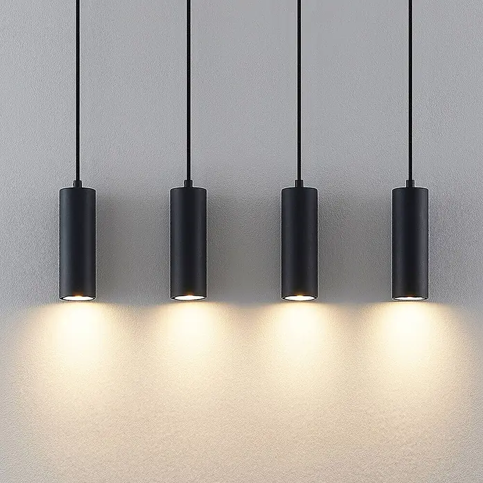 Lindby Pendelleuchte Maniva - L x B x H: 60 x 8 x 18 cm, schwarz, holz hell, Schwarz, GU10 - Vier schwarze zylindrische Pendelleuchten hängen an Kabeln und strahlen warmes Licht nach unten ab.