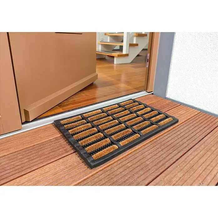 Astra Fußmatte RiminiSchwarz/Natur, 40 x 60 cm, 70% Kokos, 30 % Gummi - Fußmatte aus Kokosfaser vor einer geöffneten Haustür auf einer Holzterrasse, ideal zum Sauberhalten des Eingangsbereichs.
