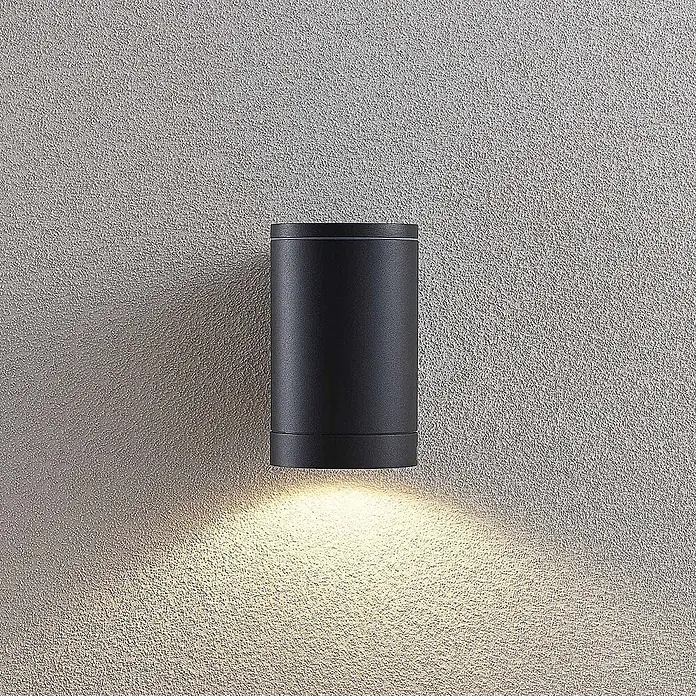 Lucande Außenwandleuchte Thomke - alu / grau / zink, alu / grau / zink, IP65 - Schwarze zylindrische Up-Down-Wandleuchte an einer strukturierten Wand, strahlt warmes Licht nach unten.