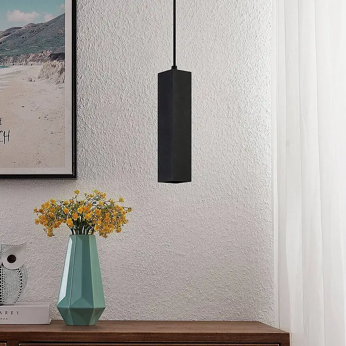 Prios Pendelleuchte Neliyah - L x B x H: 5,6 x 5,6 x 25 cm, schwarz, sandSchwarz, GU10 - Eine schwarze rechteckige Pendelleuchte hängt von der Decke in einem modernen Raum und beleuchtet den Bereich über einer Holzkommode.